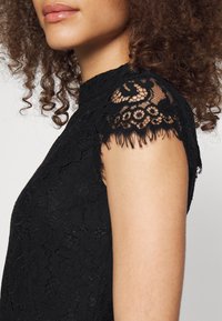 Černý krajkový top s krátkými rukávy s vlnitým okrajem, složitými květinovými vzory a přiléhavým střihem.