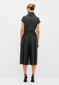 Grå, åtsittande topp med hög krage, tillsammans med vida, veckade culottes. Bärs med svarta högklackade skor. Slät textur, minimalistisk design.