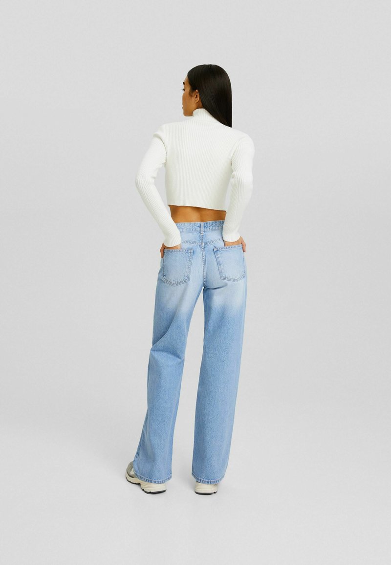 Crop top blanc à côtes avec manches longues, associé à un jean large bleu clair avec deux poches arrière et une finition délavée.
