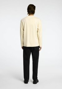 Svetlo bež srajca z dolgimi rokavi v kombinaciji s črnimi kavbojkami. Srajca ima preprost dizajn, ohlapen kroj in gladko teksturo.