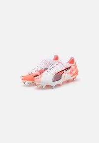 White and neon orange soccer cleats with a textured upper, black accents, and five metal studs on each sole for traction.