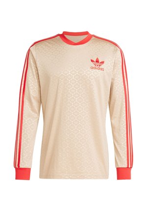 Chemise beige à manches longues avec un motif géométrique, des rayures rouges sur les manches et un logo adidas brodé sur la poitrine gauche.