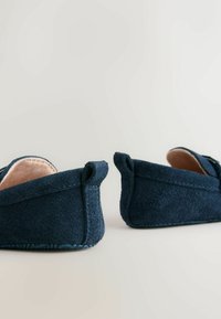 Tumesinine seemisnahast poolsaapad, millel on sile sisemus ja dekoratiivne õmblus. Madala profiliga, polsterdatud sisetald ja väikesed silmusega kontsakaunistused.