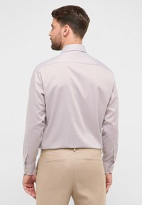 Gestreept shirt met lange mouwen in lichtbeige en bruin met een aangesloten kraag. De achterkant heeft een schouderstuk en manchetten met knopen. Draagt goed bij beige broek.