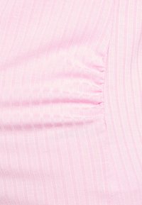 Tecido rosa claro com riscas verticais. O material parece suave, com um leve brilho. O detalhe franzido ao longo da borda adiciona textura.