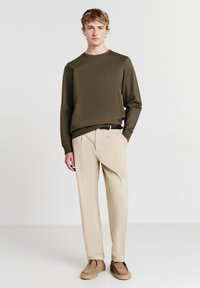 Camicetta a maniche lunghe verde oliva, pantaloni beige e scarpe slip-on color tan. Tessuto morbido e leggero con un design semplice e un taglio rilassato.