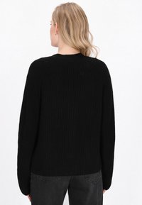 Maglione nero a maglia con texture a coste, spalle abbassate e scollatura rotonda. Indossato con jeans grigio scuro per un contrasto.