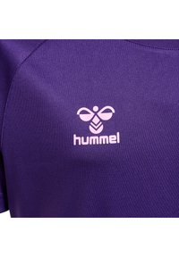 Lilla sportskjorte lavet af tekstureret stof, med et lys rosa "hummel" logo og et bie-grafik på brystet. Korte ærmer.