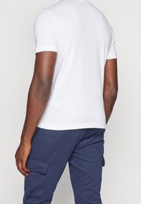 Bílé tričko s krátkým rukávem a kulatým výstřihem, hladká textura a volný střih, kombinováno s námořnickými cargo kalhotami s bočními kapsami.