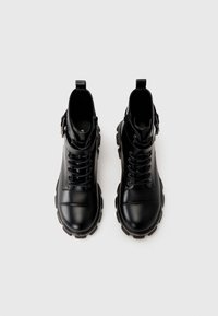 Black ankle boots made of smooth leather with a rounded toe. Features laces, metal accents, and a thick rubber sole with a textured finish.