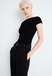 Črn rebrast kratkotrajen top v kombinaciji z visokimi črnimi hlačami, ki imajo pas z srebrnimi očesi. Enostaven, eleganten dizajn in prilegajoč silhueta.