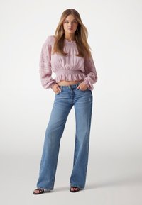 Top scurt de culoare roz deschis, cu umerii goi, cu mâneci din dantelă, talie smock, asortat cu blugi evazați de culoare albastră deschisă și sandale negre cu curele.