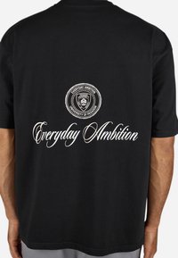 Svart bomull T-skjorte med en sirkulær logo som har "Everyday Ambition" og "University of Pegador" i hvit skrift på baksiden.