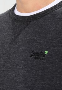 Czarny szary sweatshirt wykonany z miękkiego, teksturowanego materiału; ma okrągły dekolt i haftowane zielone logo "SuperDry" na piersi.