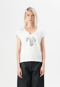 T-shirt blanc à manches courtes avec décolleté en V, arborant un design en forme de cœur à motif zèbre métallique au centre. Coupe décontractée, texture lisse.