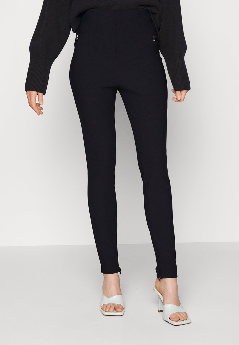 Svarta högmidjade leggings i ett stretchy material. Har sidofickor med guldfärgade detaljer. Matchas med vita öppna klackskor.