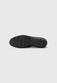 Black rubber shoe sole with a textured surface, featuring a grid pattern for traction and a slight curve at the heel.
