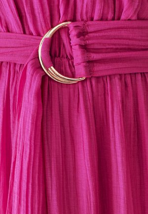 Tessuto plissettato fucsia con una fibbia a forma di mezza luna d'oro in vita. La texture è morbida, creando linee verticali in un design fluido.