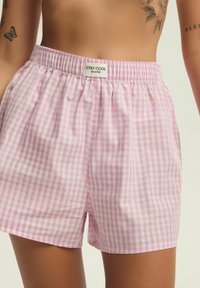 Różowe i białe spodnie w kratkę z elastycznym paskiem w talii. Materiał wydaje się lekki i przewiewny. Metka głosi "STAY COOL BLOOVII."