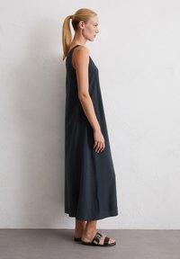 Robe maxi en gris foncé, sans manches, avec une coupe décontractée, en tissu lisse, tombant jusqu'aux chevilles. Design simple associé à des sandales à lanières noires.