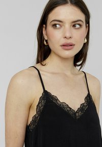 Camisole noire avec un délicat bord en dentelle florale le long du col. Bretelles fines réglables et un tissu doux et texturé.