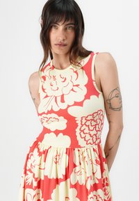 Red and cream floral dress with a fitted ribbed bodice and a flared skirt. Floral pattern features large blooms. Soft fabric texture.