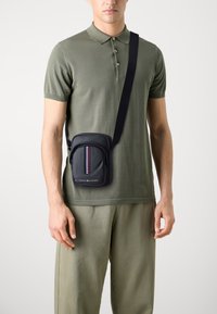 Bolso cruzado azul marino con un bolsillo frontal con cremallera, que presenta un patrón de rayas verticales en rojo, blanco y azul. Material suave y correa ajustable.
