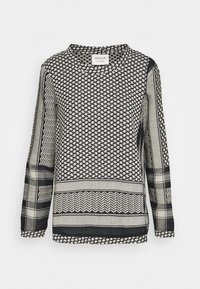 Schwarz-weißes Langarmoberteil mit gemischten geometrischen Mustern, darunter Hahnentritt, Zickzack und Karomuster, etikettiert mit Cecilie Copenhagen.