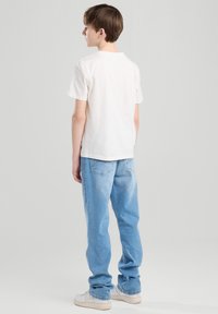 Weißes Baumwoll-T-Shirt mit Rundhalsausschnitt, getragen mit hellblauen Denim-Jeans in lockerer Passform und sichtbaren Gesäßtaschen.