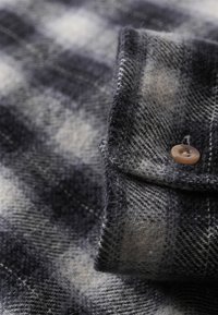 Flannel shirt featuring a gray and white plaid pattern, single-button cuff, soft texture, and a folded collar design.