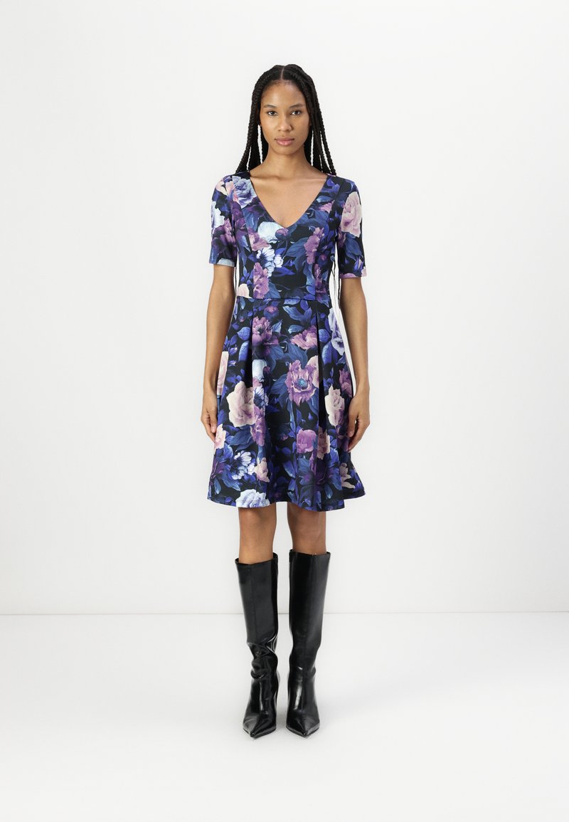 Virágmintás ruha mély V-nyakkivágással, rövid ujjal és bővülő szoknyával. Tengerészkék háttérrel rendelkezik, lila és krém színű virágokkal. Fekete, térd fölé érő csizmával viselik.