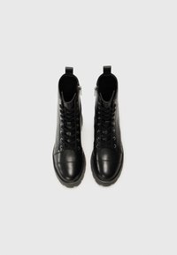 Bottes chelsea en cuir noir avec une finition lisse, dotées d'un bout arrondi, d'un laçage à l'avant, d'une fermeture éclair sur le côté et d'une semelle en caoutchouc texturée.