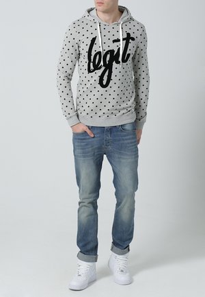 Grijze hoodie met zwarte polka dots en de tekst "legit", gecombineerd met lichtblauwe spijkerbroek en witte sneakers, die een casual stijl laat zien.