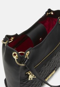 Černá kožená kabelka s prošívanou strukturou, zlatými kovovými detaily a červenou látkovou podšívkou. Obsahuje zipovou kapsu a dekorativní prvky.