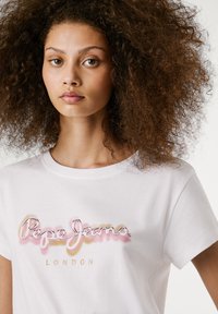 T-shirt en coton blanc avec logo "Pepe Jeans London" en rose et or, manches courtes, col rond et texture douce.