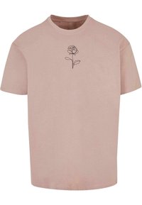 Camiseta de manga corta, de color rosa claro, hecha de algodón; presenta un dibujo de línea negra de una rosa y una hoja en la parte frontal.