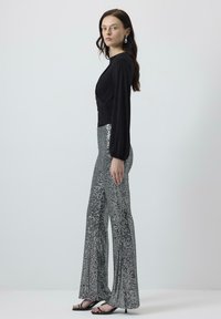 Zwarte lange mouwtop met gatherdetails en zilveren pailletten flare-broek. De soepele stof boven contrasteert met de gladde glanzende onderkant.