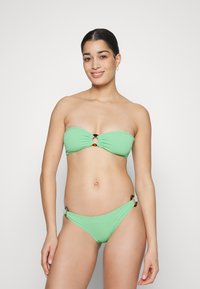 Ensemble de bikini vert comprenant un haut bandeau avec un détail en nœud et des accents en écaille de tortue, associé à un bas de bikini assorti.