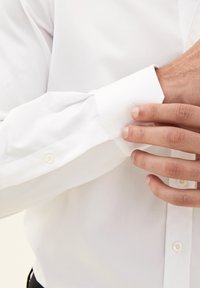 Witte overhemd met lange mouwen van een gladde stofafwerking, voorzien van een knoopmanchet en subtiele stikdetails op de mouw.
