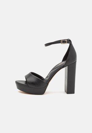 Mustat nahkaiset korolliset sandaalit, joissa on paksu neliönmuotoinen korko ja nilkkahihna. Päällisosassa on ristiinkietoutuva muotoilu ja sileä pinta.