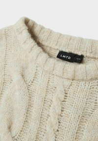 Pull en maille torsadée couleur crème, avec un col rond, un tissu texturé et une étiquette marquée "LMTD" taille 13-14.