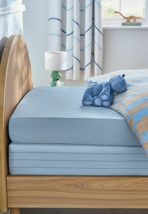 Kinderbett mit blau gestreiftem Matratze und Kissen, blauem Plüschnilpferd-Spielzeug, hölzernem Kopfteil, Seitenlampe und Fenster mit Vorhängen.