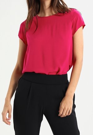 Blusa fucsia a maniche corte con scollatura rotonda, abbinata a pantaloni neri a vita alta con dettagli plissettati sul davanti.