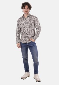 Camicia button-up a maniche lunghe con motivo floreale in bianco e nero; abbinata a jeans in denim blu e sneakers beige. Tessuto morbido e leggero.