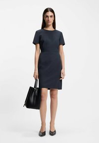 Short-sleeved, fitted navy dress with a round neckline and an A-line silhouette. Paired with a black leather tote and pointed-toe heels.