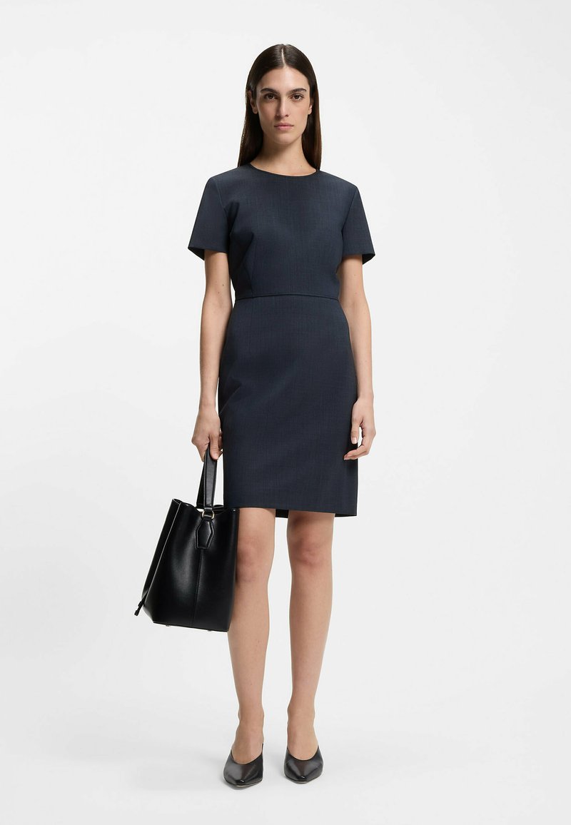 Short-sleeved, fitted navy dress with a round neckline and an A-line silhouette. Paired with a black leather tote and pointed-toe heels.