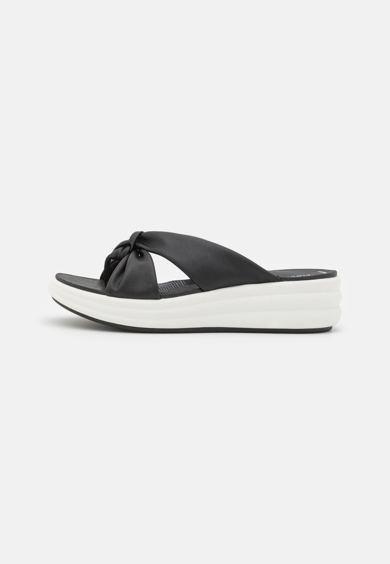Sandalias de cuero negro con diseño de tiras anudadas y suela de plataforma blanca acolchada. La suela cuenta con un patrón texturizado para mayor agarre.