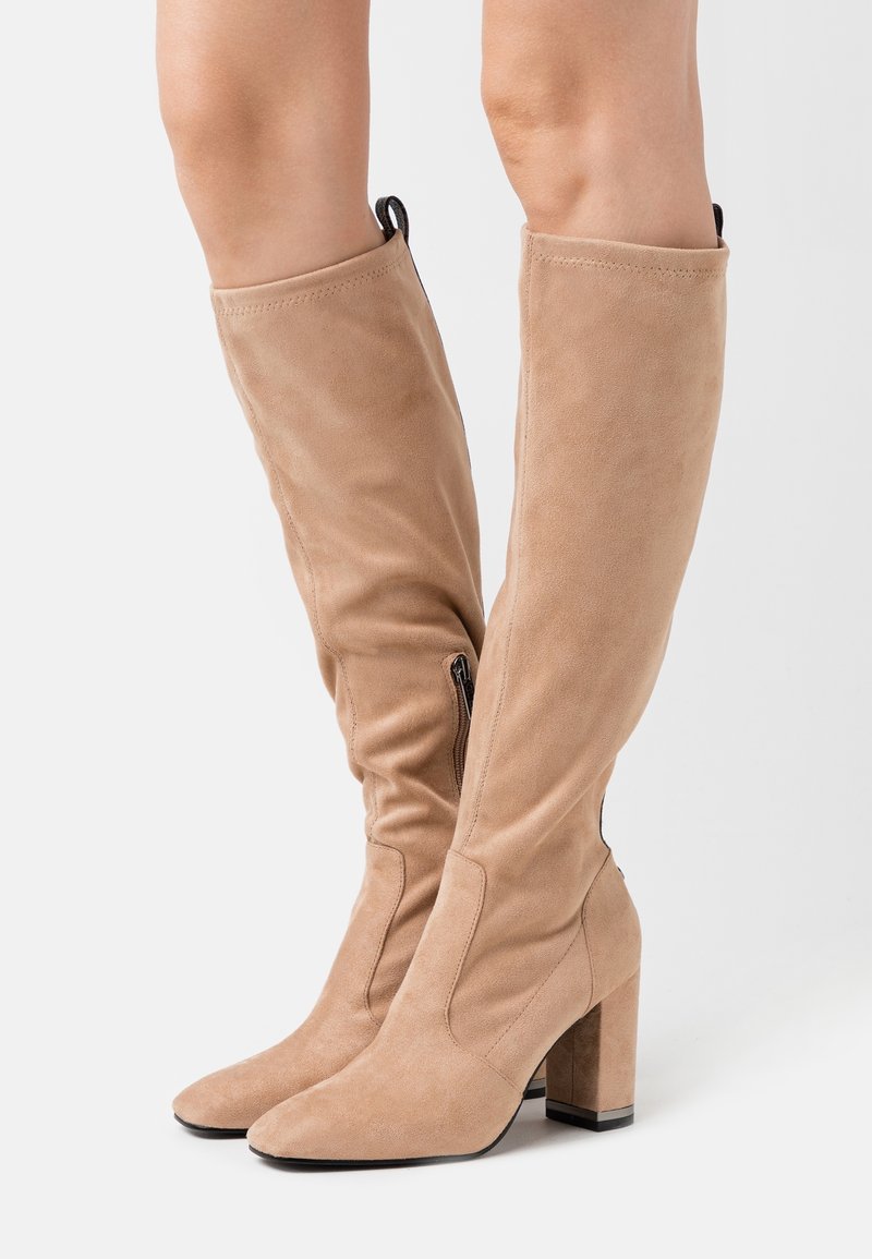 Bottes en suède beige jusqu'aux genoux avec un bout pointu et un talon carré, dotées d'une fermeture éclair sur le côté et d'une languette pour un enfilage facile.