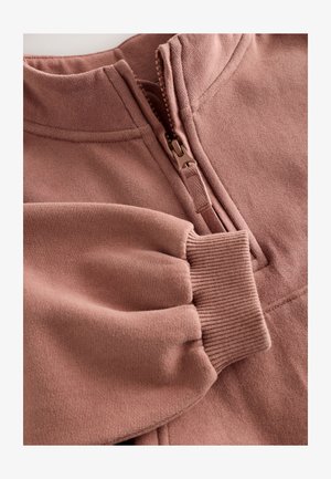 Roza flis pulover s polukopčanim ovratnikom, rebrastim manšetama i glatkom teksturom. Ima strukturirani dizajn i mekanu tkaninu.