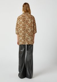Übergrößiges, kurzärmliges Hemd in Beige mit Leopardenmuster, kombiniert mit weit geschnittenen, hochgeschnittenen schwarzen Lederimitathosen.